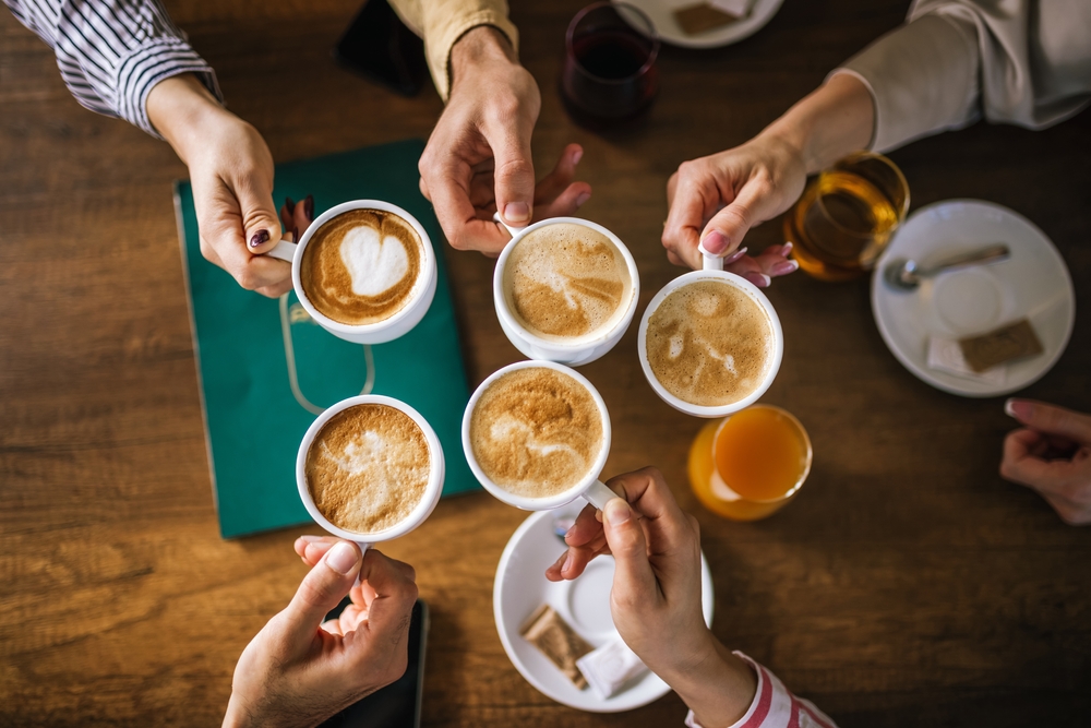 Grupa osób trzymających filiżanki kawy nad stołem w kawiarni