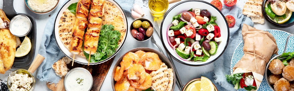 Grecka kuchnia i przekąski na stole: souvlaki, krewetki, sałatka grecka z fetą, oliwki i pita