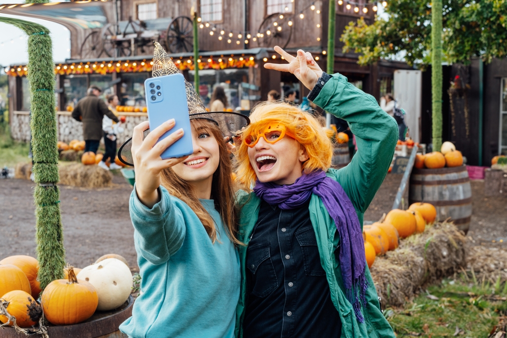 Dwie kobiety robią selfie wśród dyń i jesiennych dekoracji na farmie dyniowej
