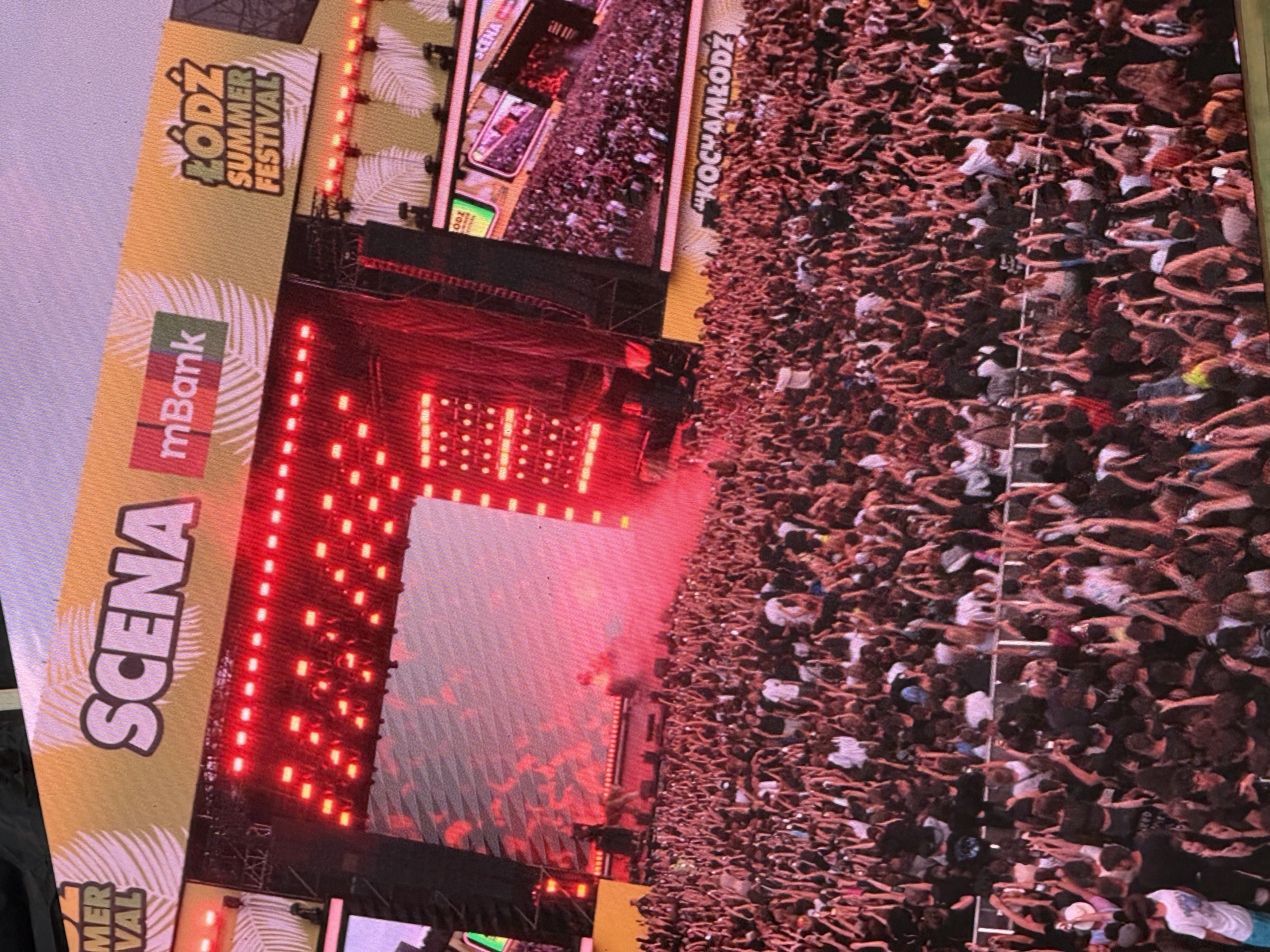 Artysta występujący na czerwono oświetlonej scenie Łódź Summer Festival przed tłumem publiczności.