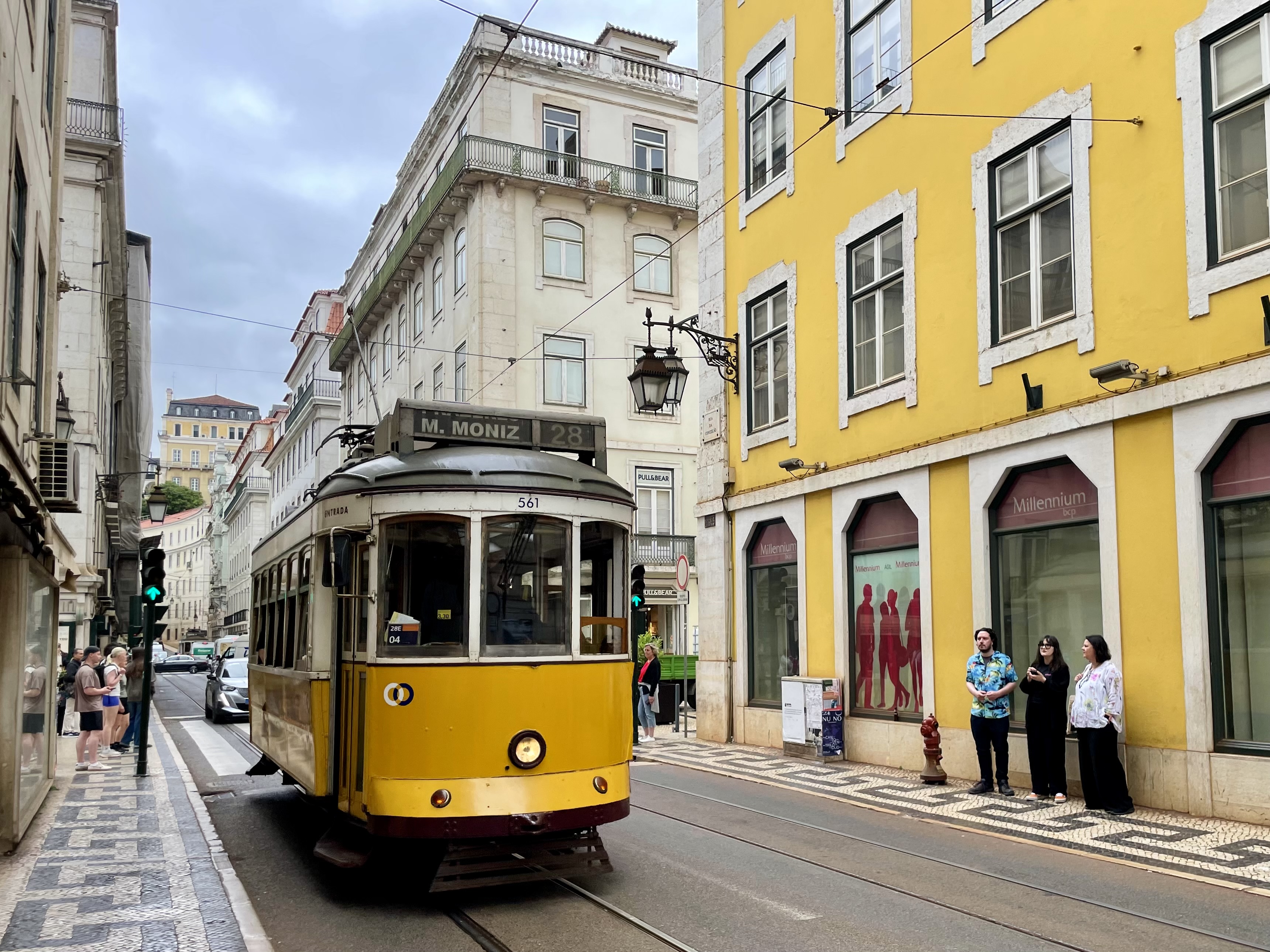 Żółty zabytkowy tramwaj numer 28 jedzie wąską ulicą Lizbony między kamienicami i kolorowymi fasadami.