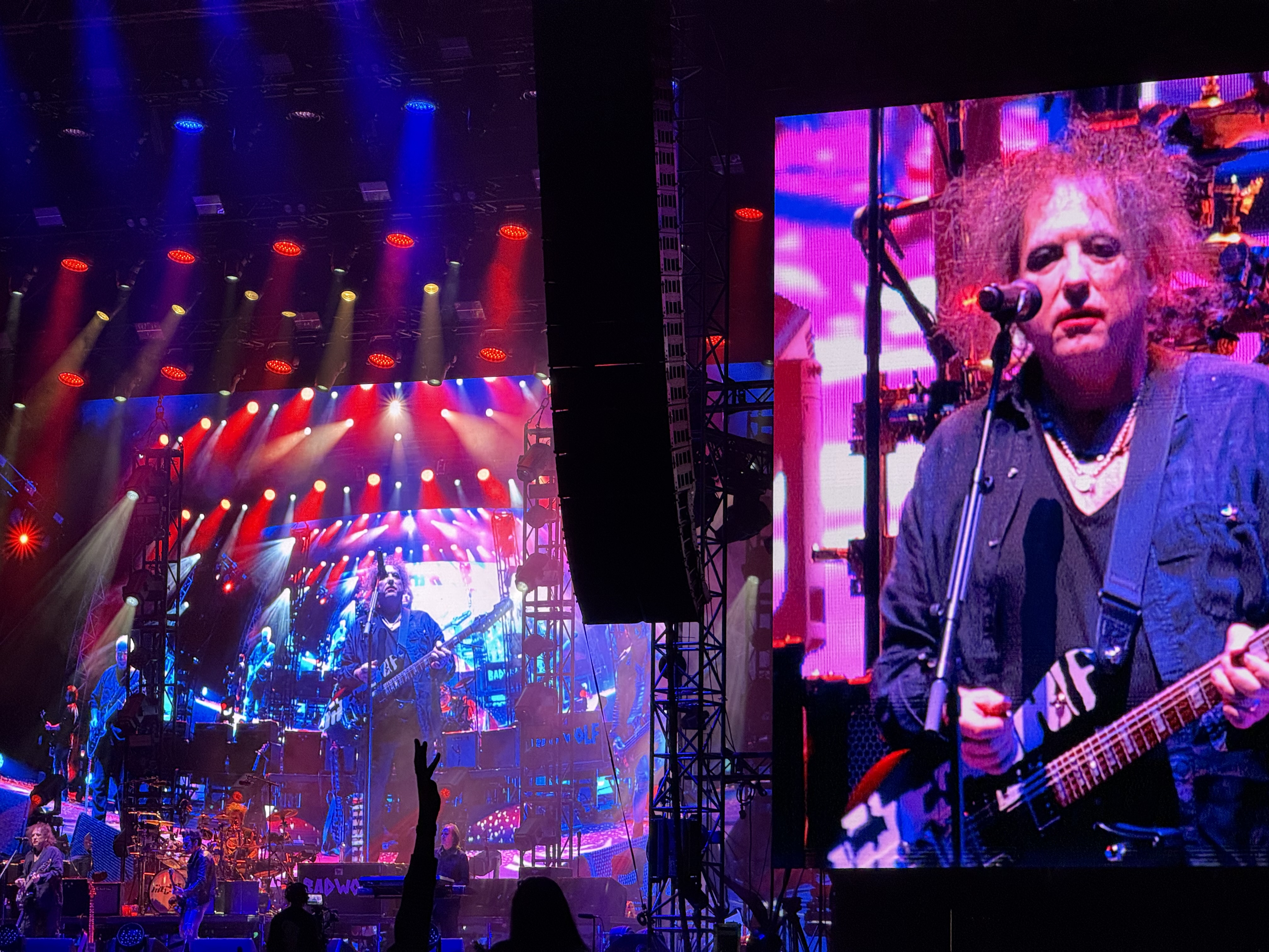 Koncert The Cure na festiwalu Pohoda, scena oświetlona czerwonym i niebieskim światłem, a na wielkim ekranie wokalista grający na gitarze.
