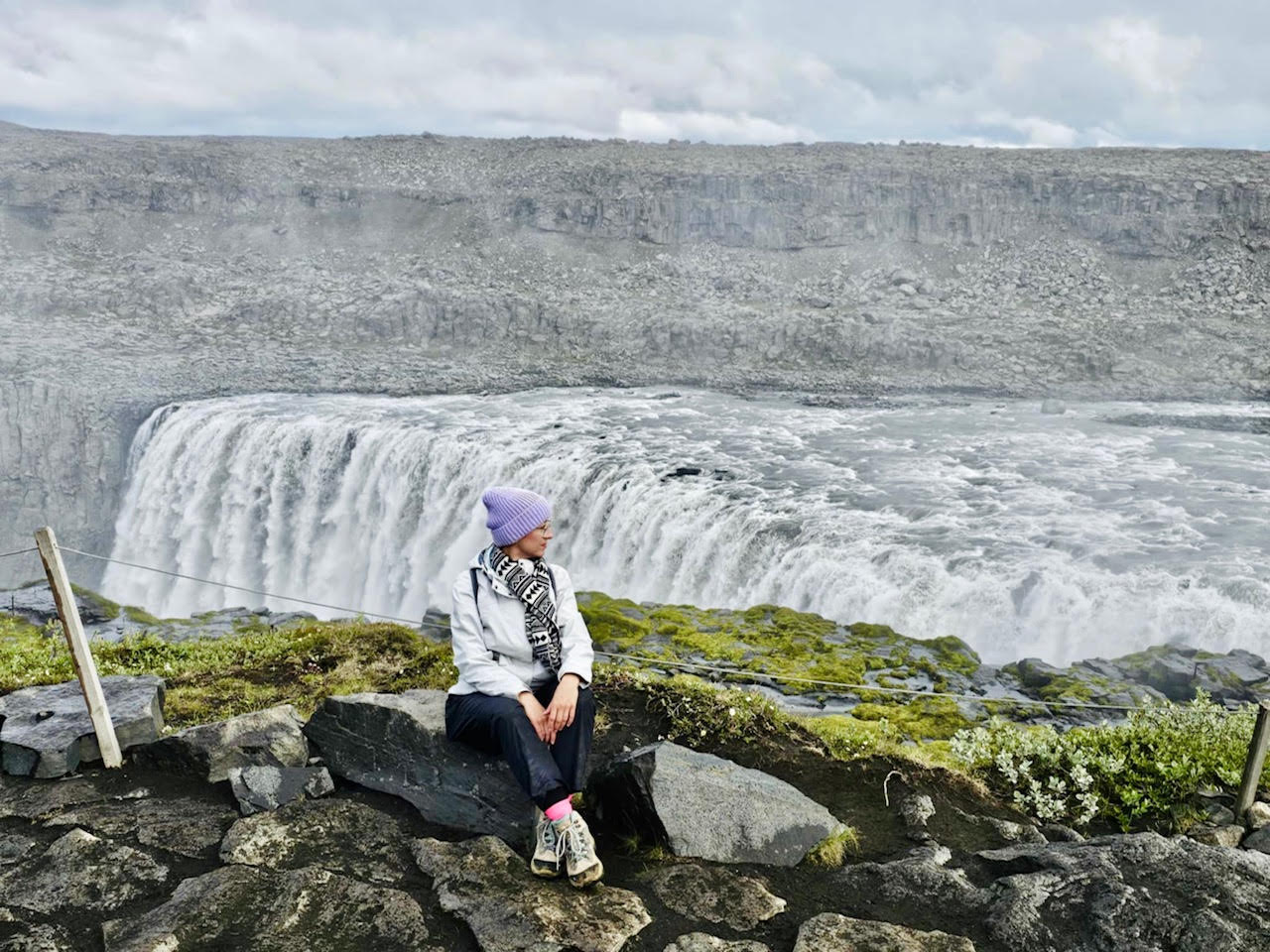 Autorka siedząca na skałach przy potężnym wodospadzie Dettifoss na Islandii.