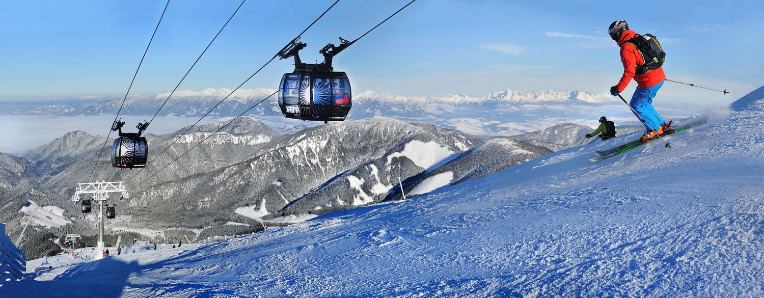 Narciarze na trasie w Jasnej pod Chopokiem, obok gondoli i panoramicznego widoku na ośnieżone góry