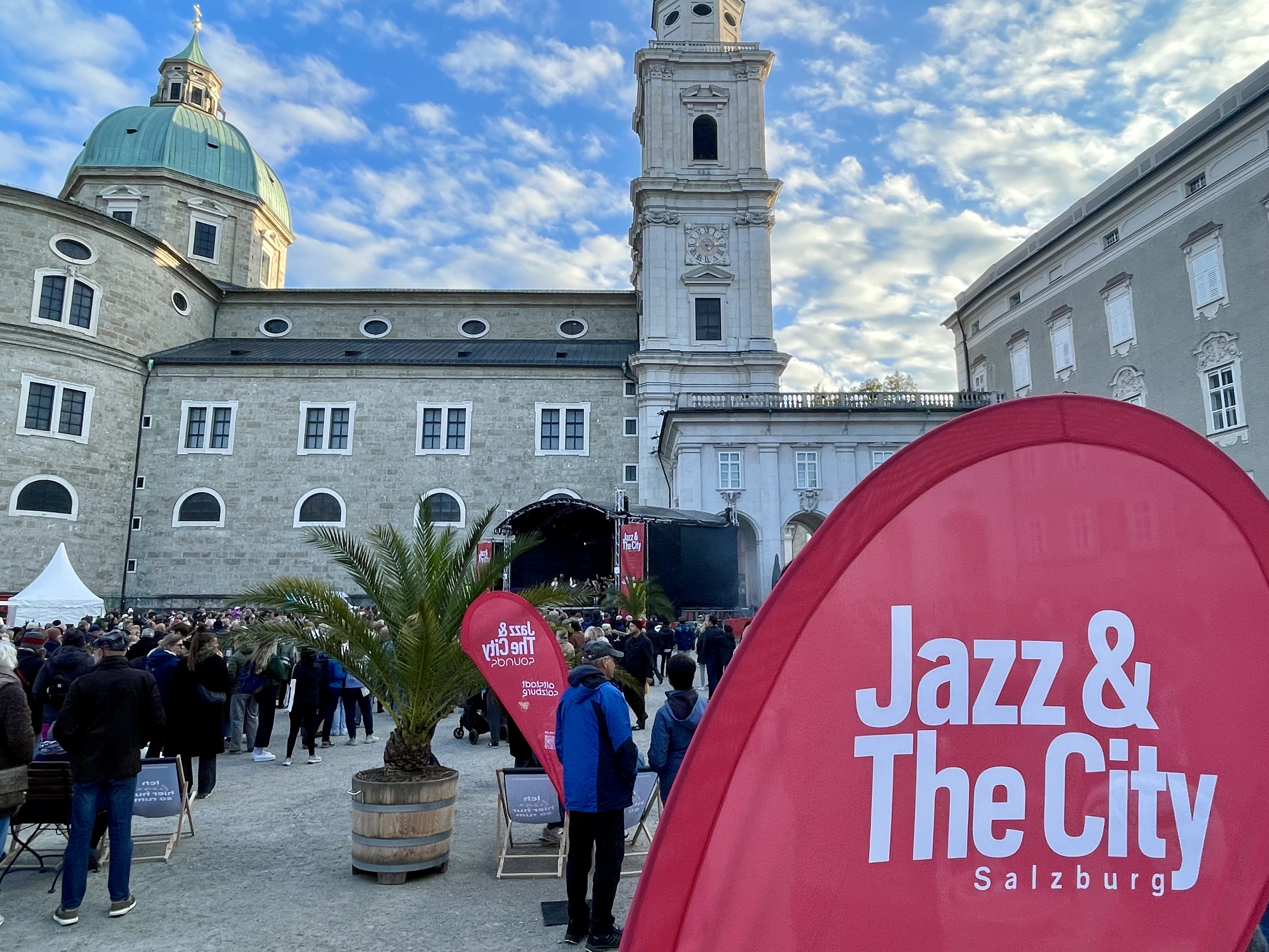 Tłum ludzi na placu Residenzplatz w Salzburgu podczas festiwalu Jazz&TheCity, w tle katedra i scena koncertowa.