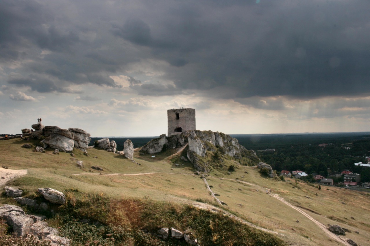 Kamienna wieża zamku w Olsztynie wznosząca się na wapiennej grani pod burzowym niebem.