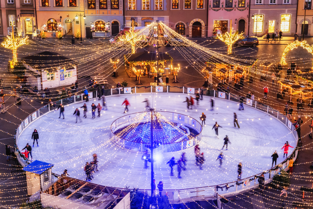 Widok z góry na oświetlone lodowisko na Rynku Starego Miasta w Warszawie, z licznymi łyżwiarzami i świątecznymi światłami.