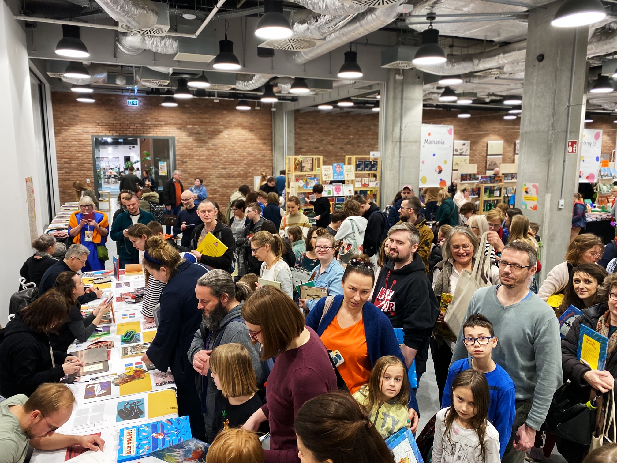 Publiczność podczas wydarzenia Mały Koneser w Butelkowni w Centrum Praskim Koneser w Warszawie, dzieci i dorośli siedzą i stoją podczas spotkania.