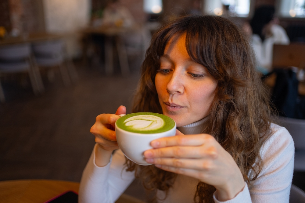 Kobieta pije matcha latte z charakterystyczną zieloną pianką w kawiarni.