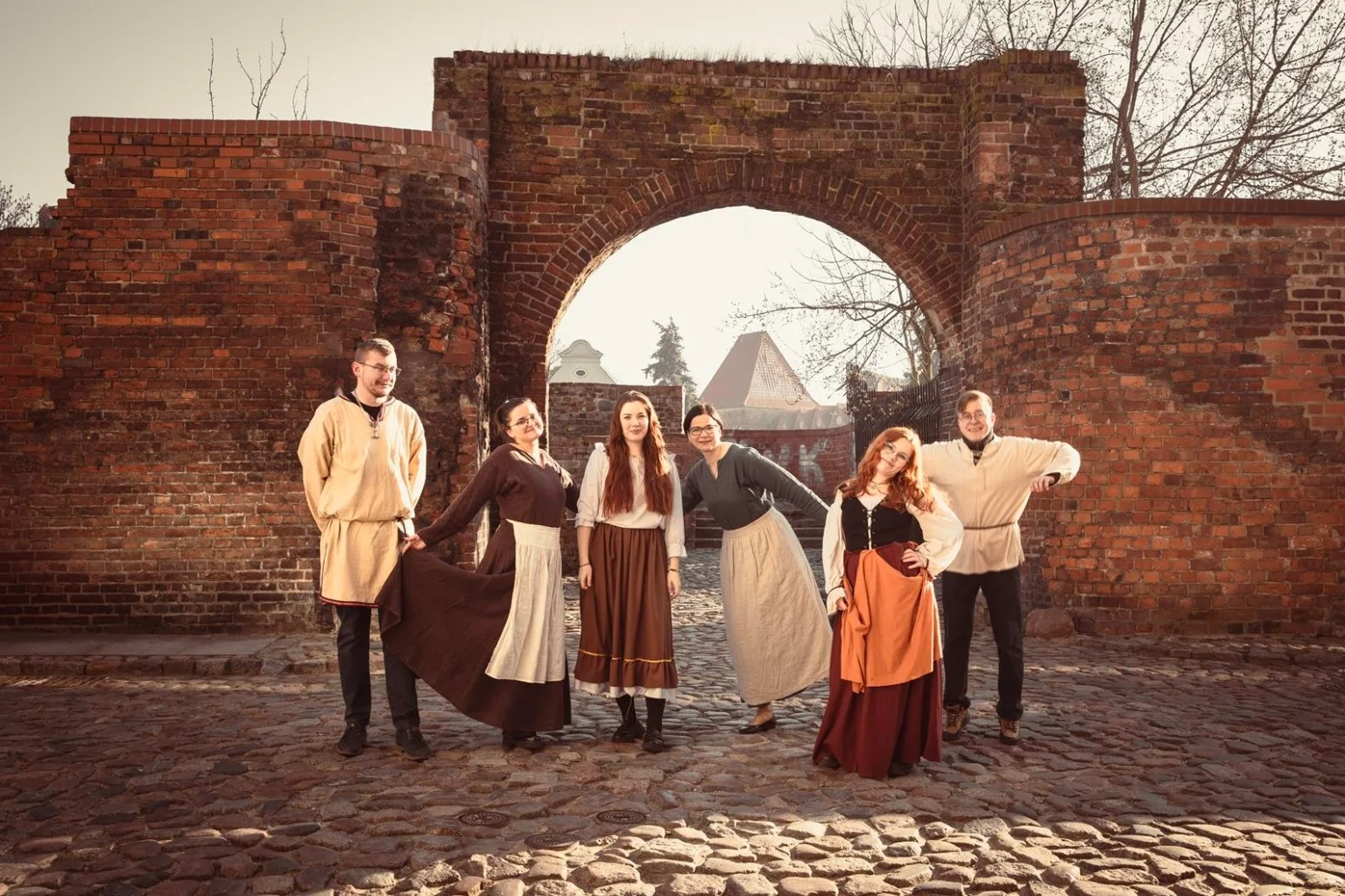 Zespół Muzeum Historii Partaczy w Toruniu w historycznych strojach przy gotyckiej bramie toruńskiej starówki
