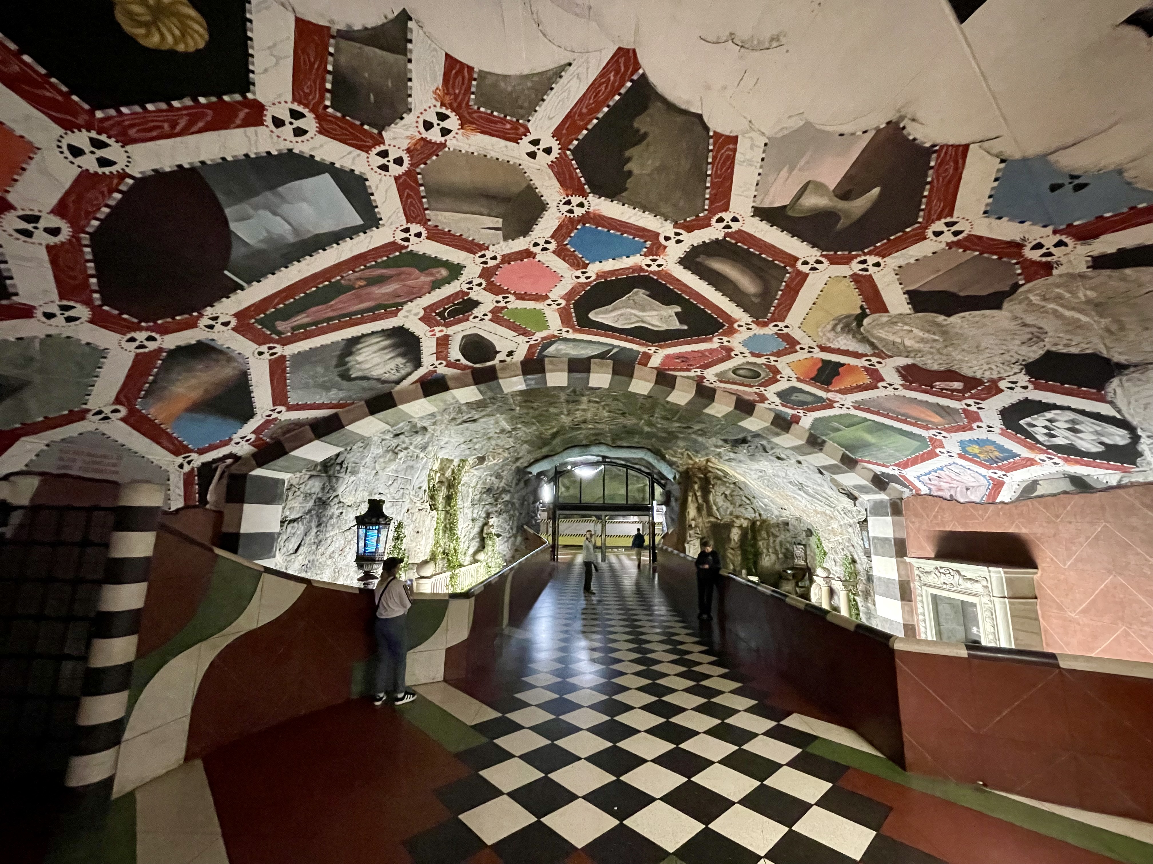 Kolorowy hol stacji Kungsträdgården z szachownicową posadzką, skalnymi ścianami i dekorowanym sklepieniem.