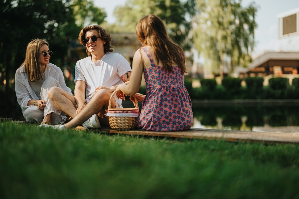 Piknik na trawie w parku pod Warszawą troje przyjaciół siedzi na kocu na trawie z koszykiem