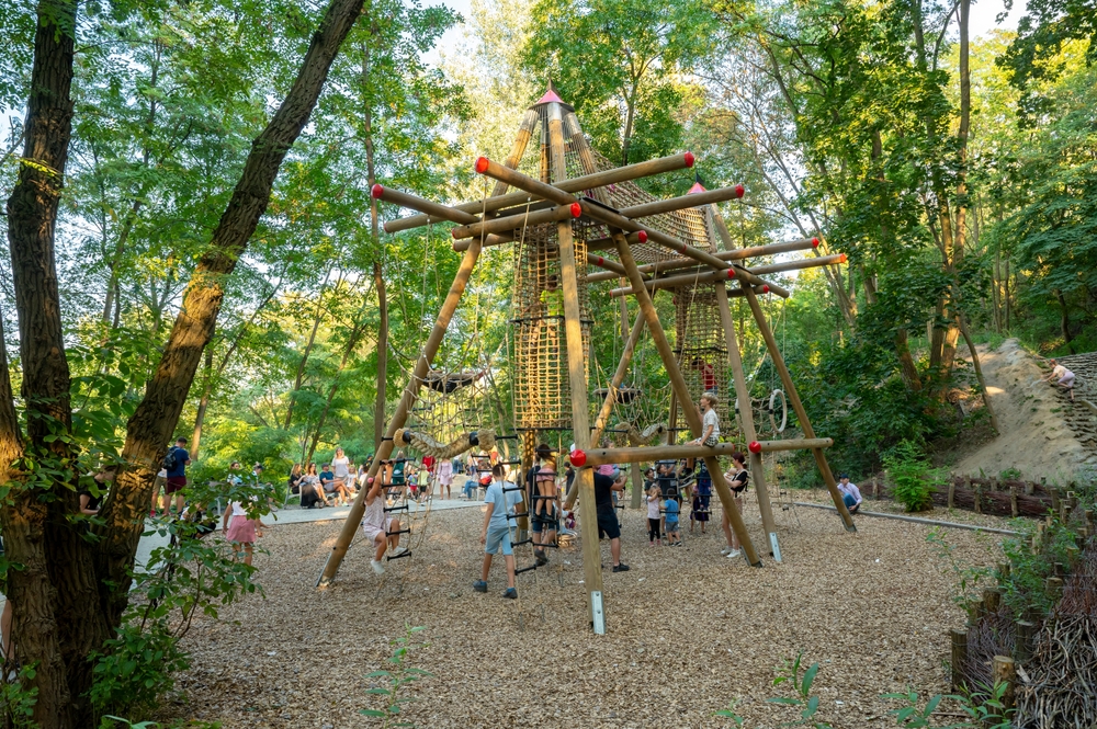 Drewniana konstrukcja wspinaczkowa na placu zabaw wśród drzew w Warszawie.
