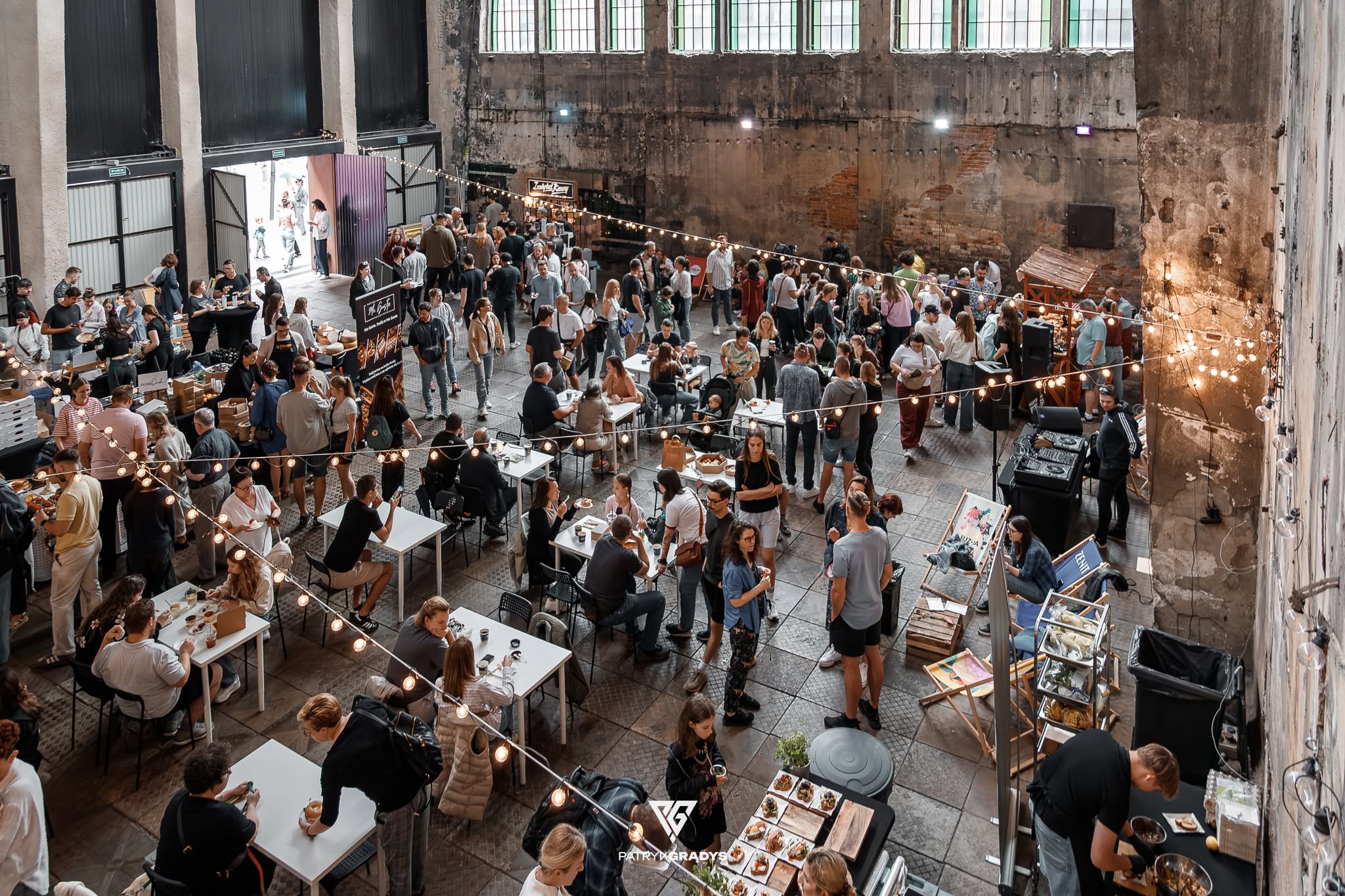 Tłum ludzi przy stolikach i stoiskach gastronomicznych w industrialnym wnętrzu dawnej fabryki