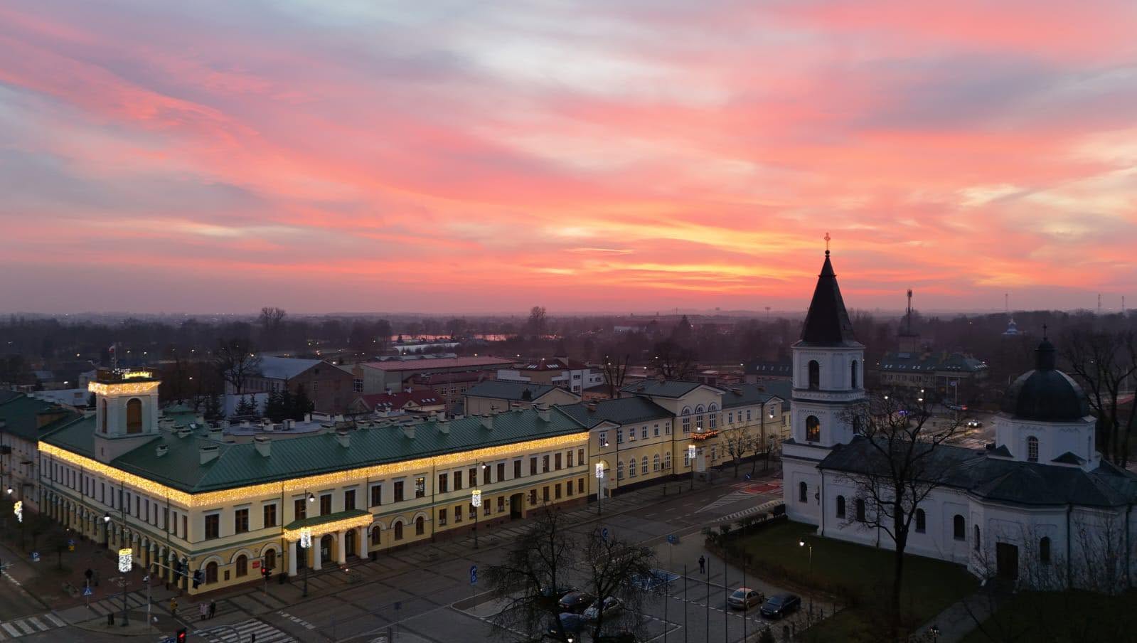 Centrum Suwałk widziane z góry o zachodzie słońca, z zabytkową zabudową, kościołem i różowym niebem nad miastem.