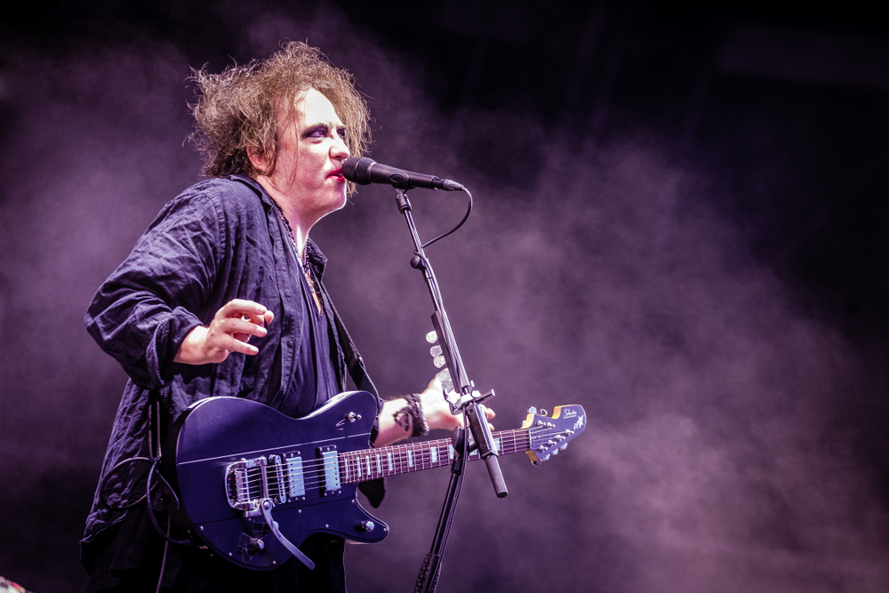 Wokalista The Cure śpiewa i gra na gitarze podczas koncertu