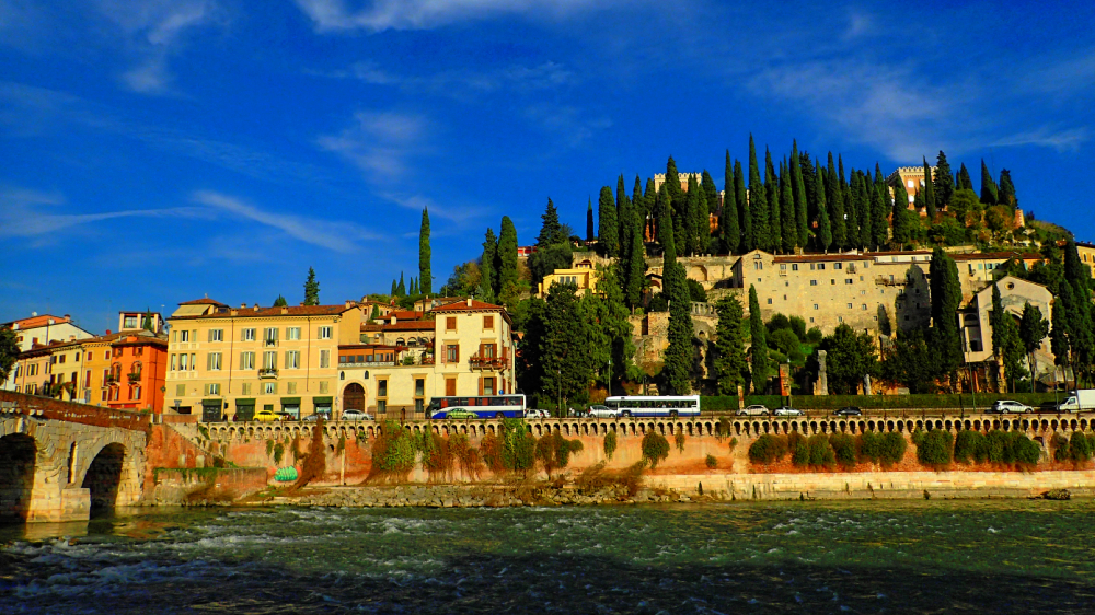 Panorama Werony nad rzeką Adygą z mostem i wzgórzem porośniętym cyprysami oraz historyczną zabudową.