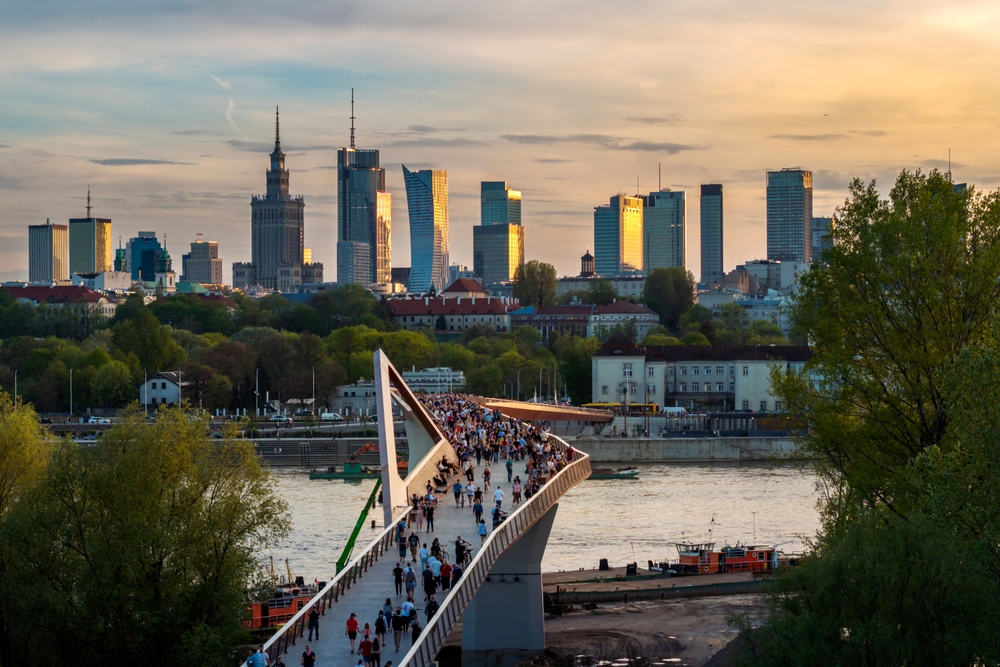 Kładka pieszo-rowerowa nad Wisłą w Warszawie, spacerujący ludzie i panorama miasta.