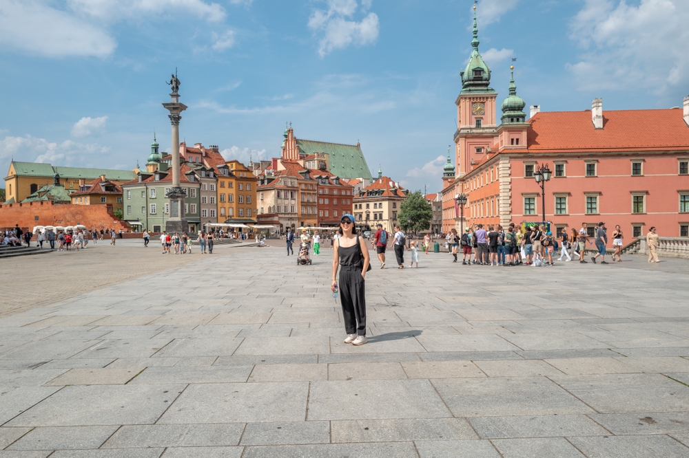 Plac Zamkowy w Warszawie z widokiem na Zamek Królewski, kolumnę Zygmunta i spacerujących turystów w majowy dzień.