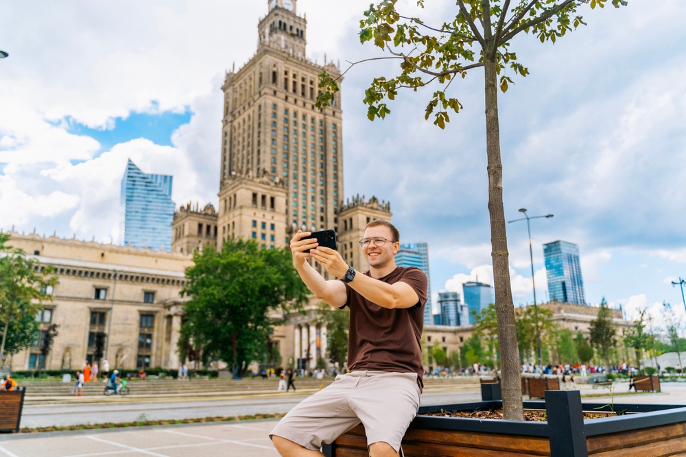 Mężczyzna robiący zdjęcie telefonem przed Pałacem Kultury i Nauki w Warszawie