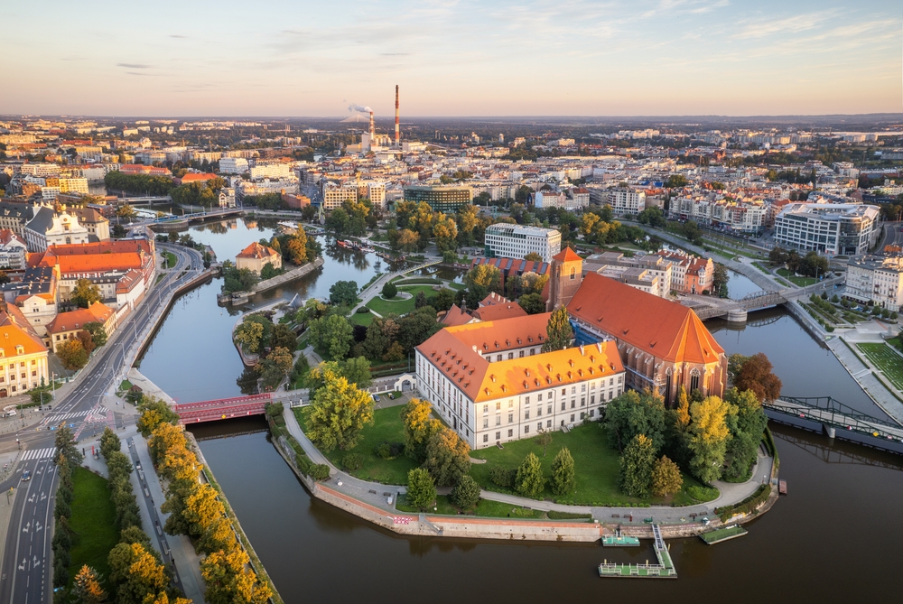 Widok z góry na wyspę otoczoną ramionami Odry, zabytkowy kościół, czerwone dachy, mosty i centrum Wrocławia.