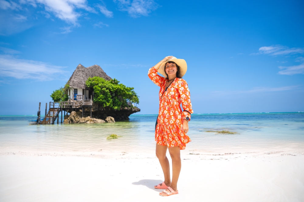 Kobieta w pomarańczowej sukience stoi na plaży przy restauracji The Rock na Zanzibarze.