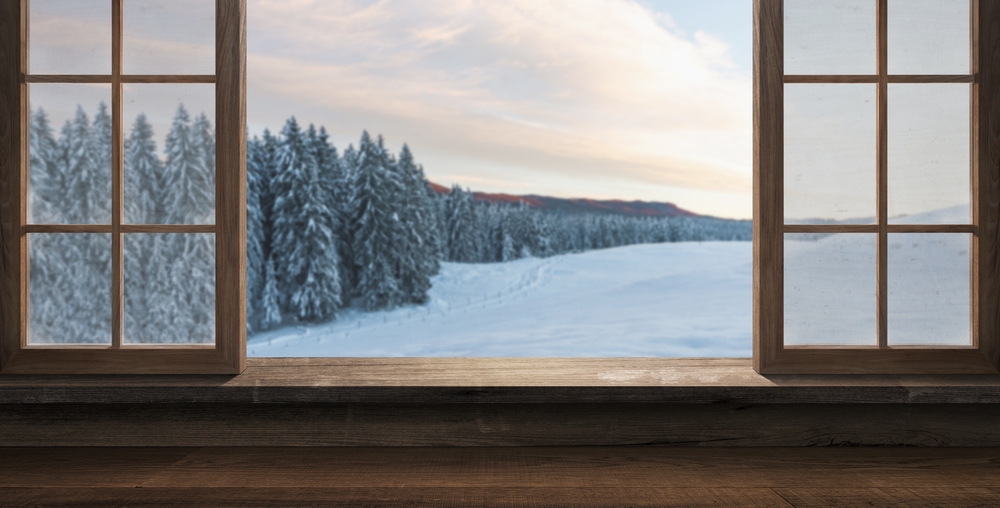 Widok przez drewniane okno na ośnieżony las i zimowy krajobraz o świcie.